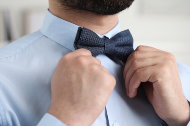 Photo of Man in shirt adjusting bow tie indoors, closeup