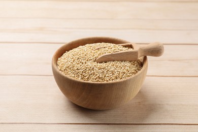 Photo of Bowl and scoop with raw quinoa on wooden table, closeup