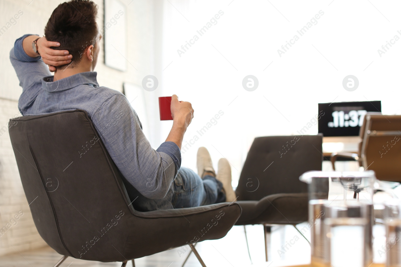 Photo of Young man with cup of drink relaxing in comfortable chair at workplace