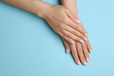 Photo of Woman showing her manicured hands with white nail polish on light blue background, top view. Space for text