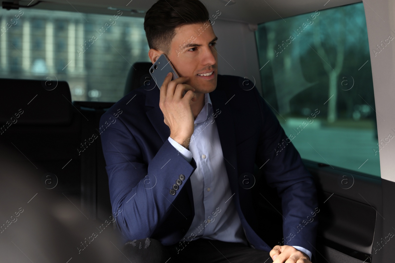 Photo of Handsome man talking on smartphone on backseat of modern car