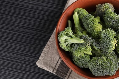 Photo of Bowl with fresh raw broccoli on black wooden table, top view. Space for text