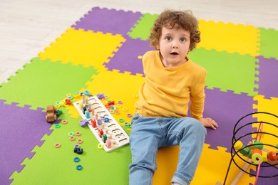 Photo of Cute little boy and different toys on puzzle mat in kindergarten