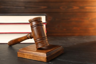 Photo of Wooden gavel and stack of books on dark textured table, closeup. Space for text