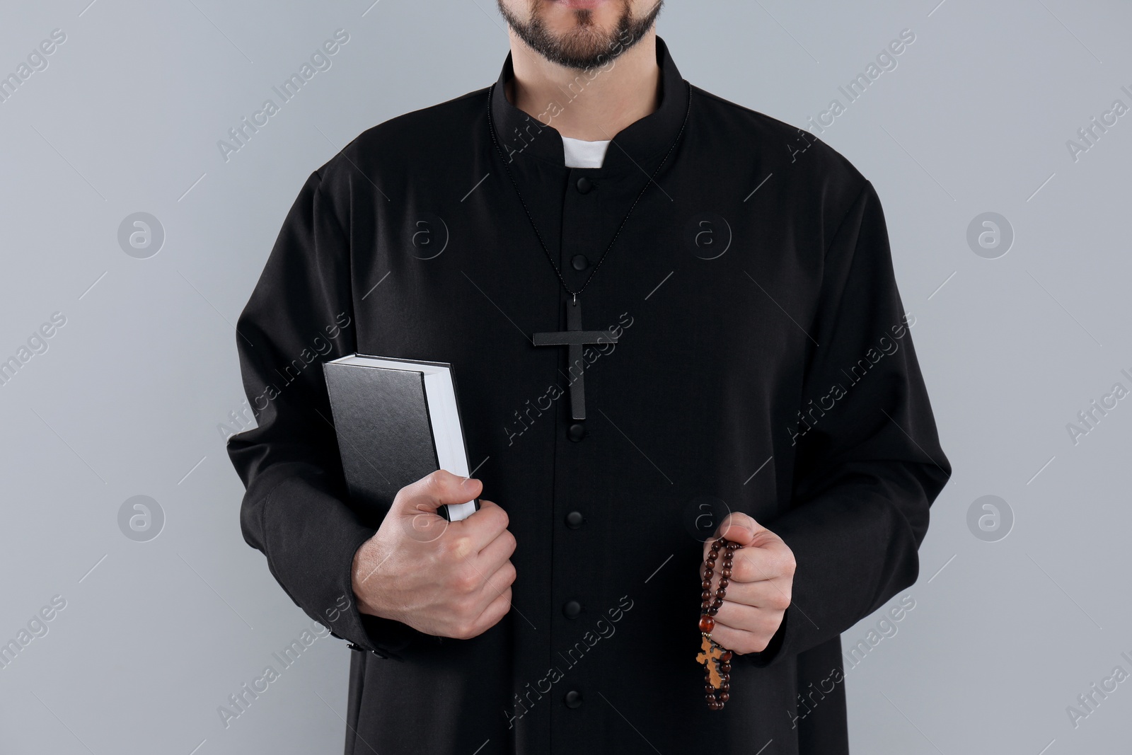 Photo of Priest with Bible and rosary beads on grey background, closeup