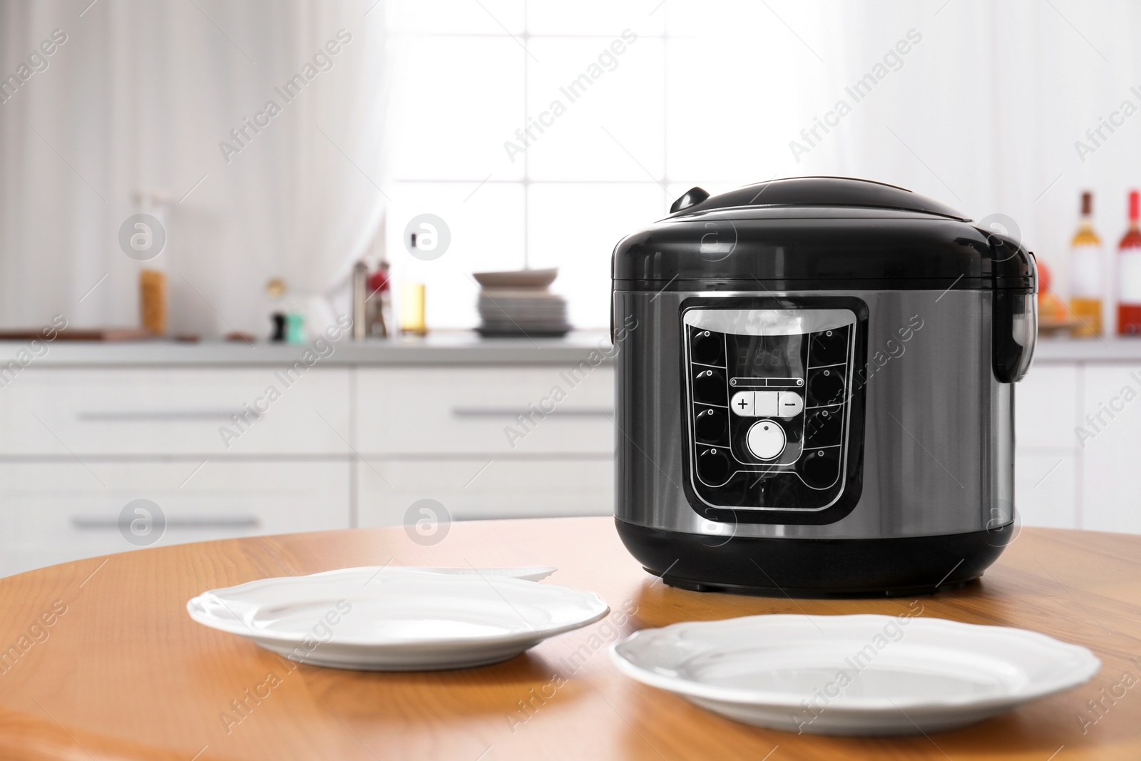 Photo of Modern multi cooker and empty plates on table in kitchen