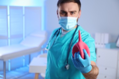 Photo of Doctor holding rubber enema in examination room, focus on hand. Space for text