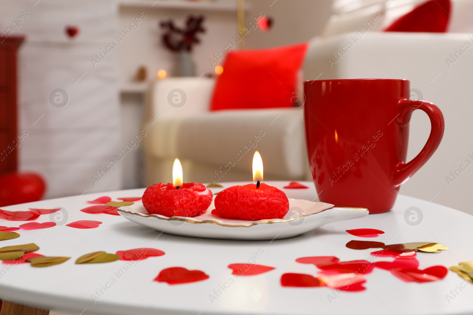 Photo of Red cup, candles and heart shaped confetti on white table indoors. Valentine's Day celebration