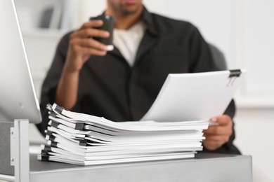 Photo of Man drinking coffee while working with documents at table in office, closeup
