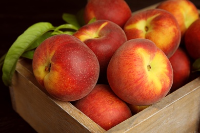 Photo of Wooden crate with tasty peaches and leaves on black background