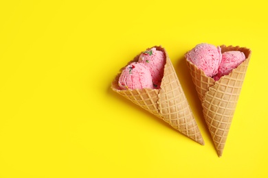 Delicious ice cream in wafer cones on yellow background, flat lay. Space for text