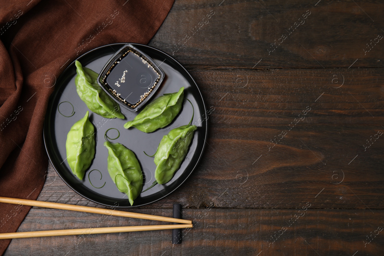 Photo of Delicious green dumplings (gyozas) with soy sauce served on wooden table, flat lay. Space for text