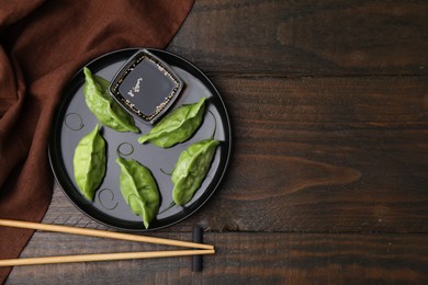 Photo of Delicious green dumplings (gyozas) with soy sauce served on wooden table, flat lay. Space for text