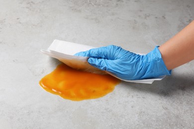 Photo of Woman wiping spilled sauce with paper towel on grey surface, closeup