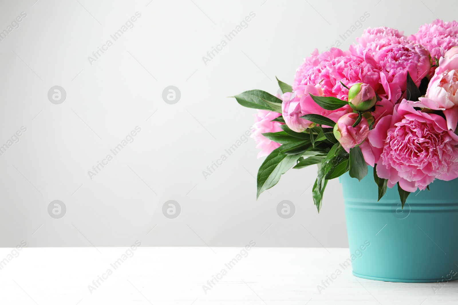 Photo of Bucket with beautiful peony flowers on table against light background