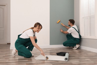 Photo of Woman applying glue onto wall paper while man hanging sheet indoors