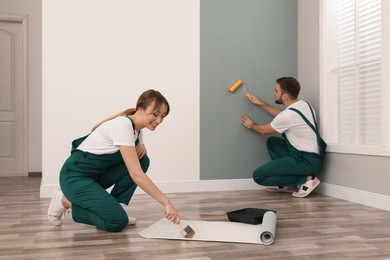 Woman applying glue onto wall paper while man hanging sheet indoors