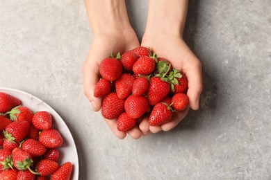 Photo of Young woman holding fresh ripe strawberries on grey background, top view