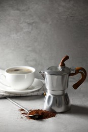 Ground coffee, moka pot and cup with drink on light grey table, space for text