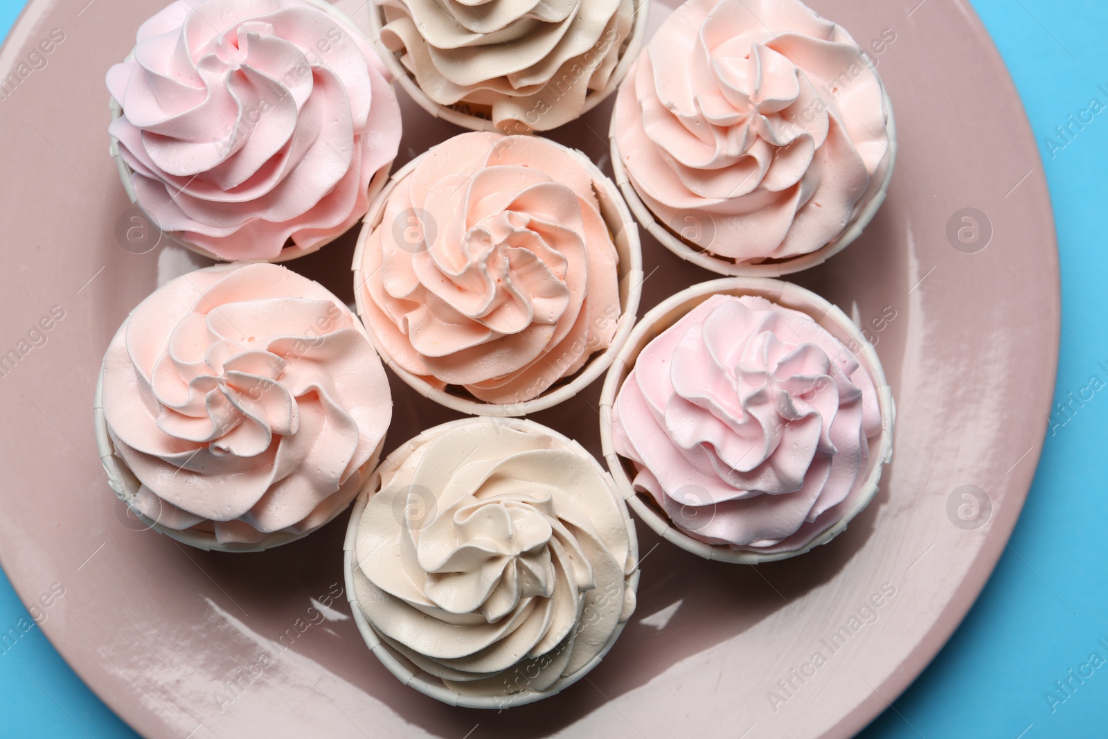 Photo of Plate with tasty cupcakes on light blue background, top view