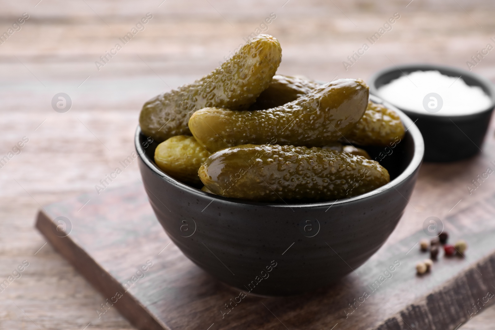 Photo of Bowl with pickled cucumbers and spices on wooden table, closeup