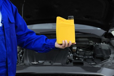 Worker holding yellow container of motor oil near modern car, closeup