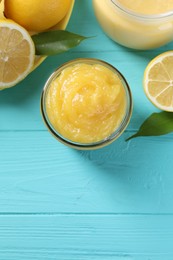 Delicious lemon curd in jar, fresh citrus fruits and green leaves on light blue wooden table, flat lay. Space for text