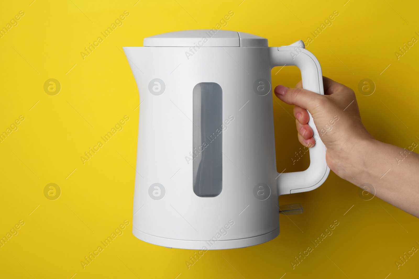Photo of Woman holding modern electric kettle on yellow background, closeup