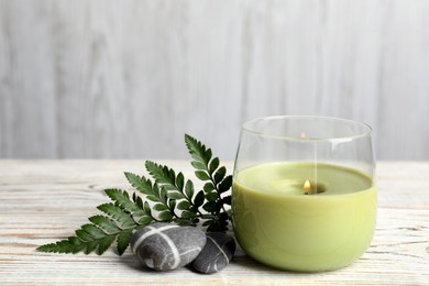 Photo of Burning candle, fern leaf and stones on white wooden table