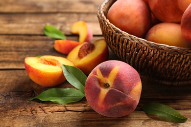 Photo of Fresh sweet peaches in wicker basket on wooden table, closeup