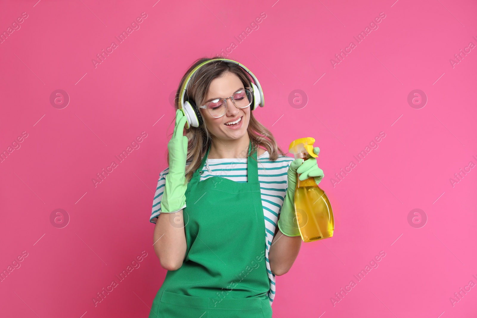 Photo of Beautiful young woman with headphones and bottle of detergent singing on pink background