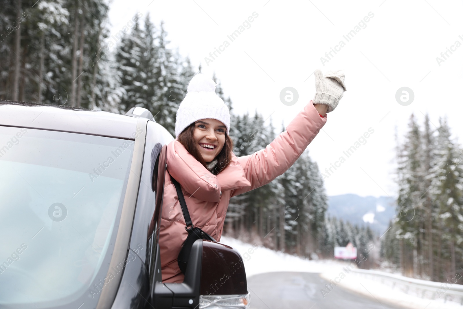 Photo of Young woman driving car and looking out of window on road. Winter vacation