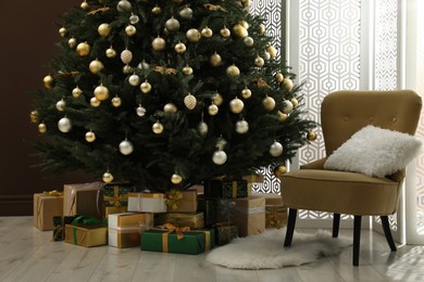 Photo of Beautifully decorated Christmas tree and many gift boxes near brown wall in room