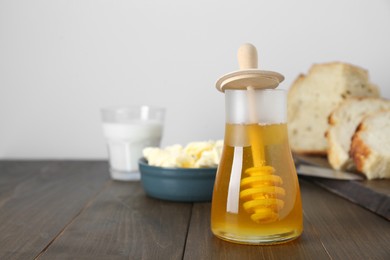 Photo of Jar of tasty honey, milk, butter and bread on wooden table. Space for text