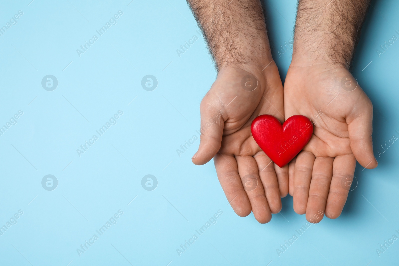 Photo of Man holding red heart on light blue background, top view. Space for text