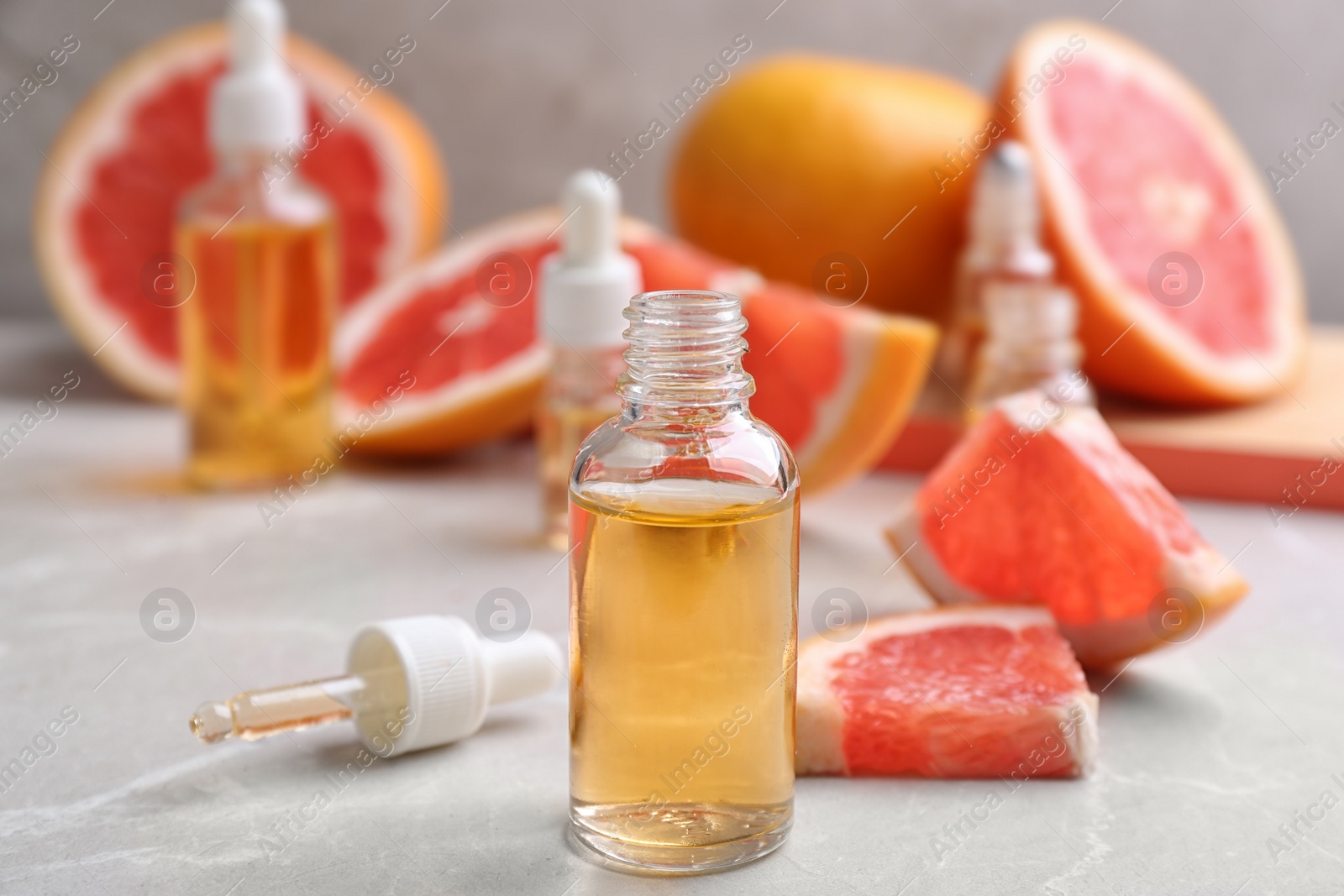 Photo of Bottles of essential oil and fresh grapefruits on grey table