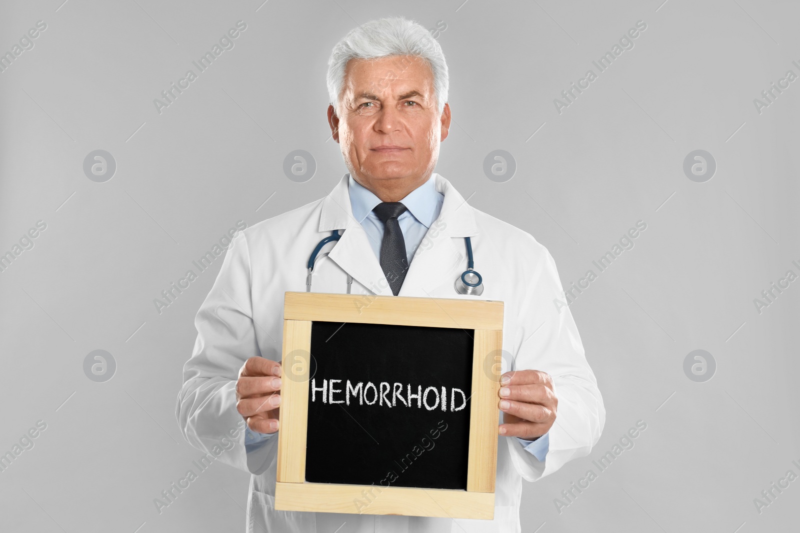 Photo of Doctor holding blackboard with word HEMORRHOID on light grey background