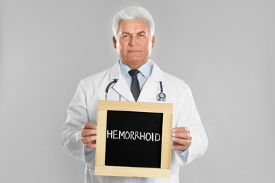 Doctor holding blackboard with word HEMORRHOID on light grey background