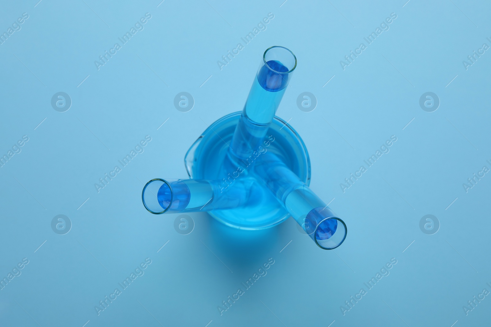 Photo of Laboratory glassware with light blue liquid on turquoise background, top view