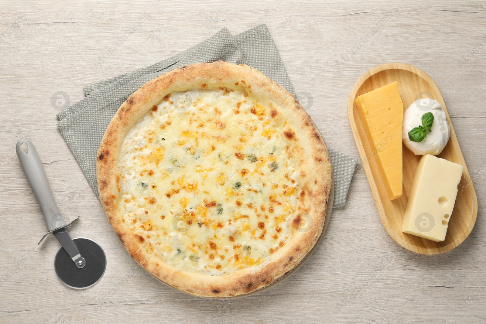 Photo of Delicious cheese pizza, cutter and different kinds of cheese on wooden table, flat lay