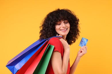 Happy young woman with shopping bags and credit card on yellow background