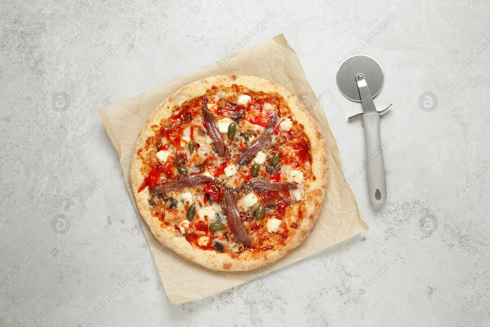 Photo of Tasty pizza with anchovies and cutter on grey table, top view