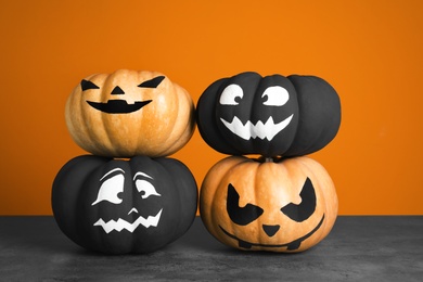 Photo of Pumpkins with scary faces on table against color background. Halloween decor