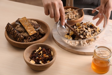 Photo of Woman preparing healthy granola bar at wooden table, closeup