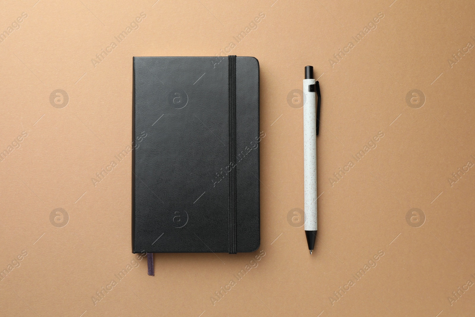 Photo of Closed black notebook and pen on light brown background, top view