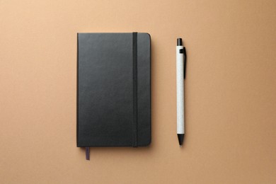 Closed black notebook and pen on light brown background, top view