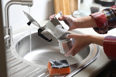 Woman washing moka pot (coffee maker) above sink in kitchen, closeup