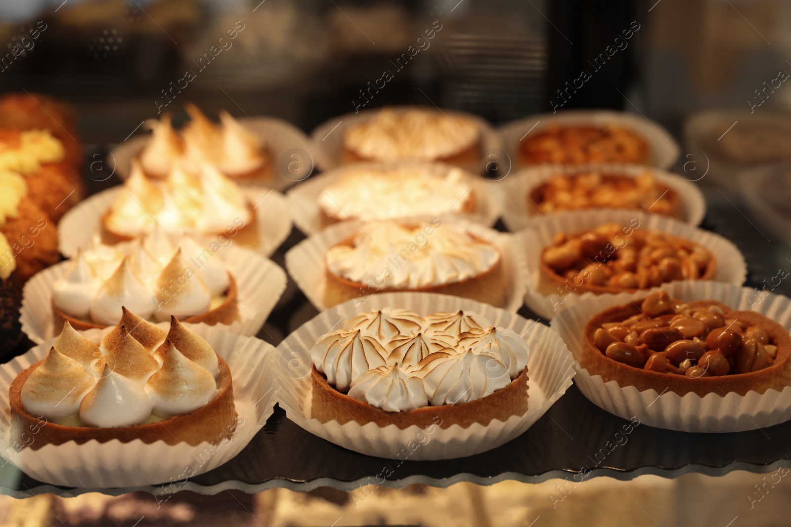 Photo of Different tasty tartlets on counter in bakery shop, closeup