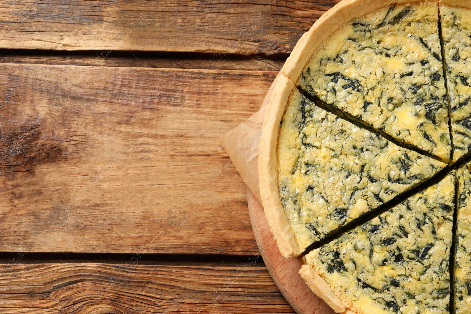 Photo of Cut delicious spinach pie on wooden table, top view. Space for text