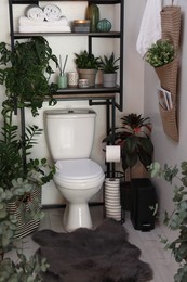 Photo of Stylish restroom interior with toilet bowl and green houseplants